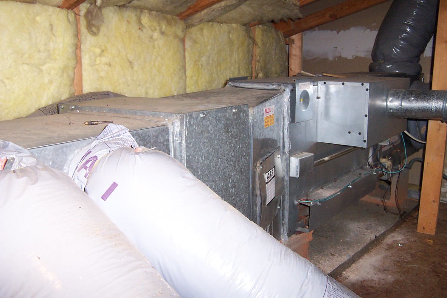 Horizontal gas furnace installed in an attic between insulated rafters, with flexible supply ducts, a metal flue pipe and the gas valve compartment