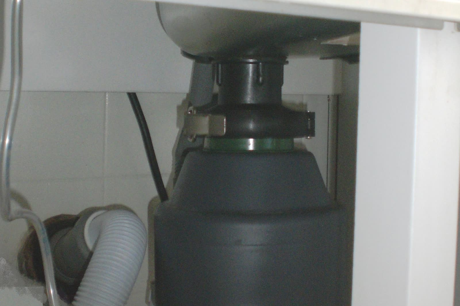Food waste disposer mounted under a kitchen sink, with the mounting ring, drain hose and power cord in the cabinet