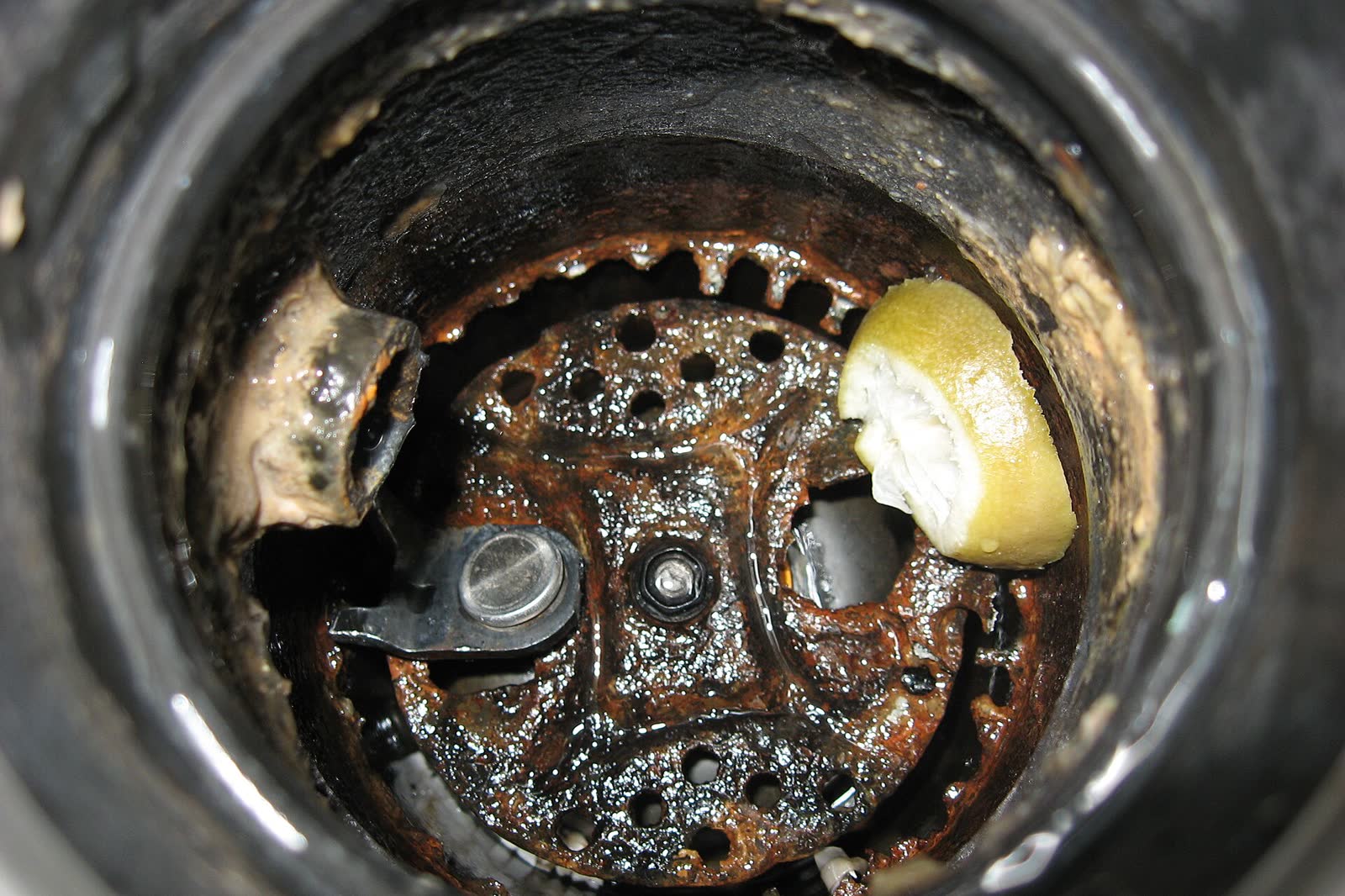 Inside a worn garbage disposal: rusty grinding plate and lugs seen from the sink