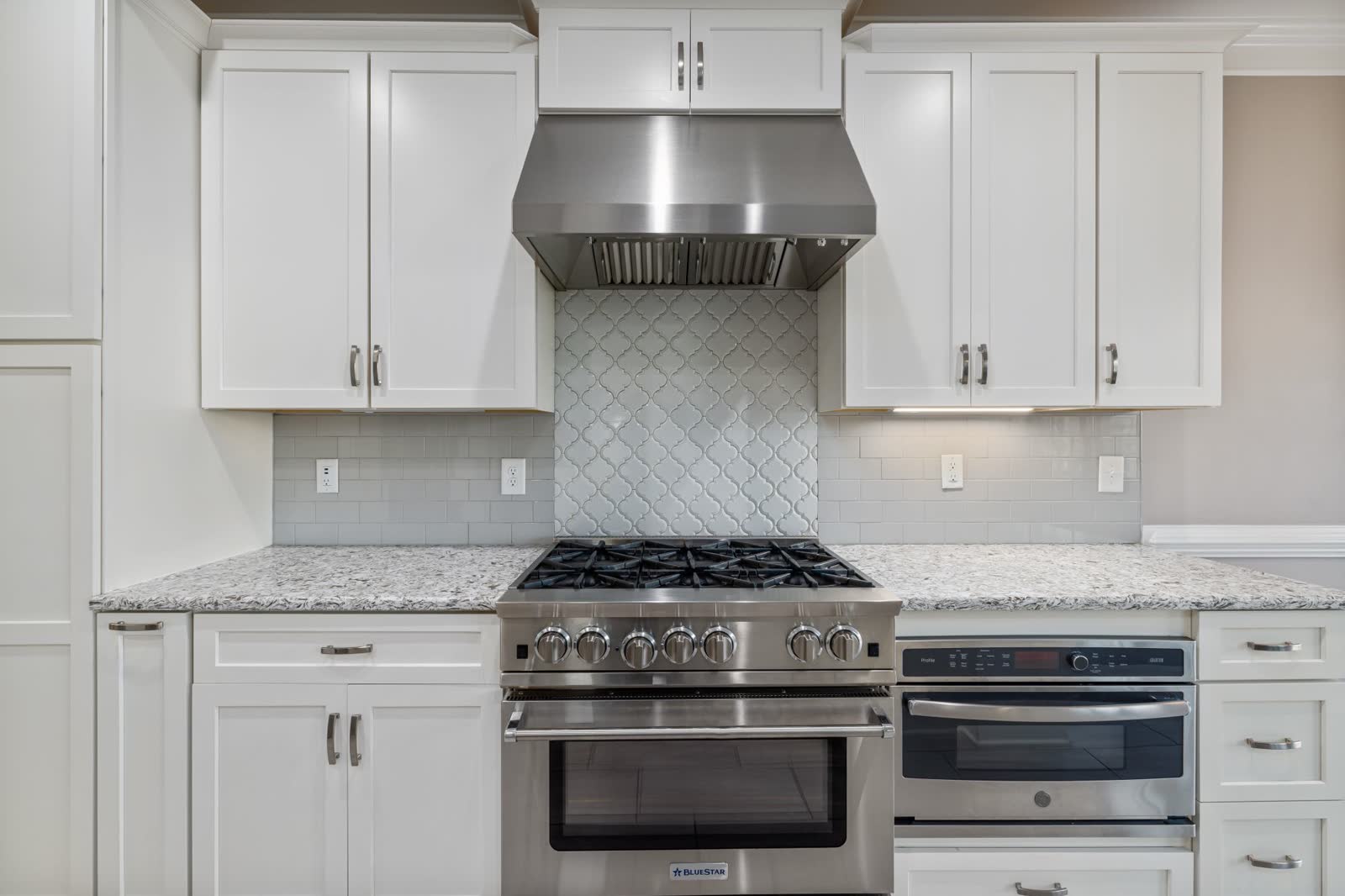 Stainless gas range with burner grates under white cabinets and a hood