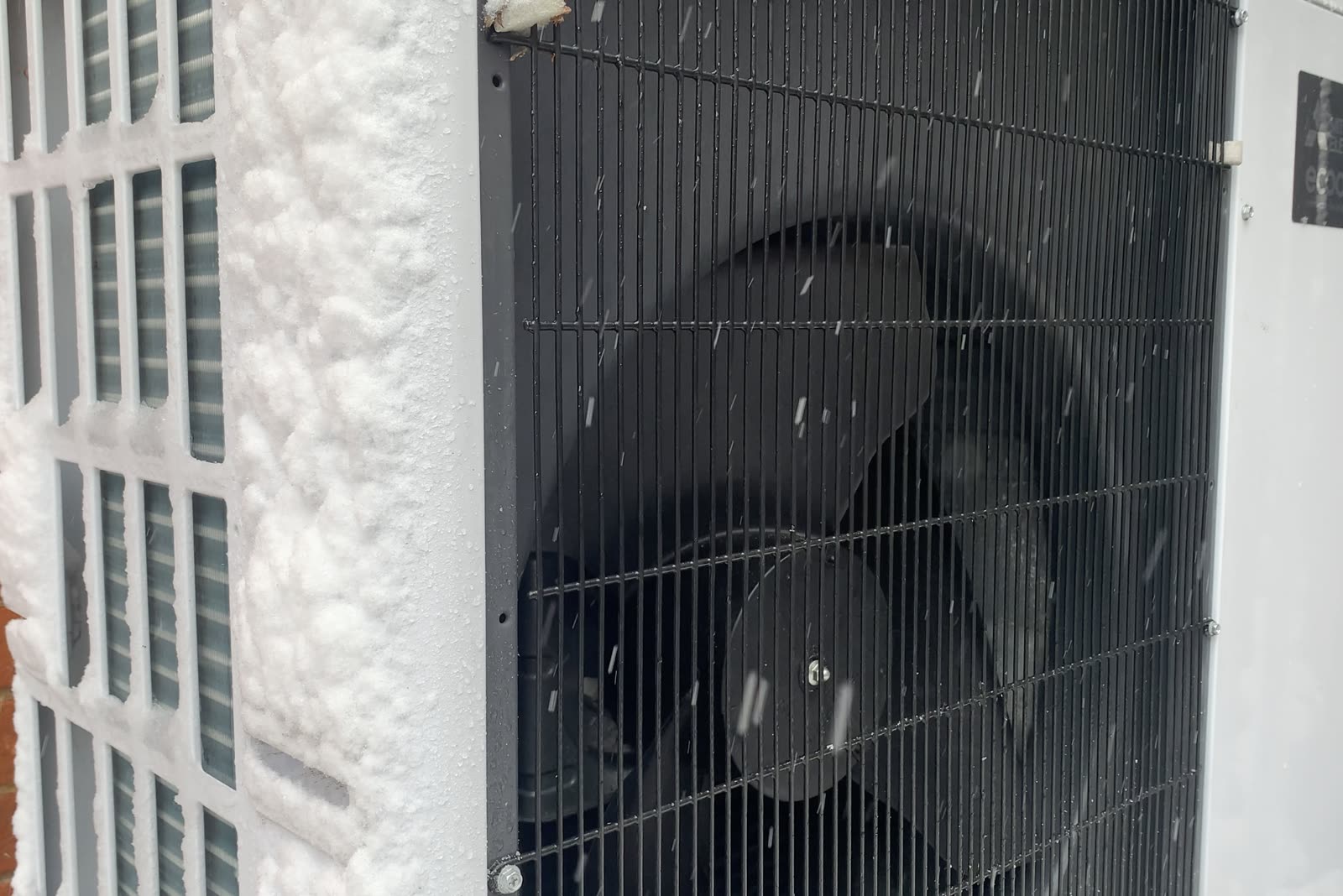 Air-source heat pump outdoor unit beside a house in the snow