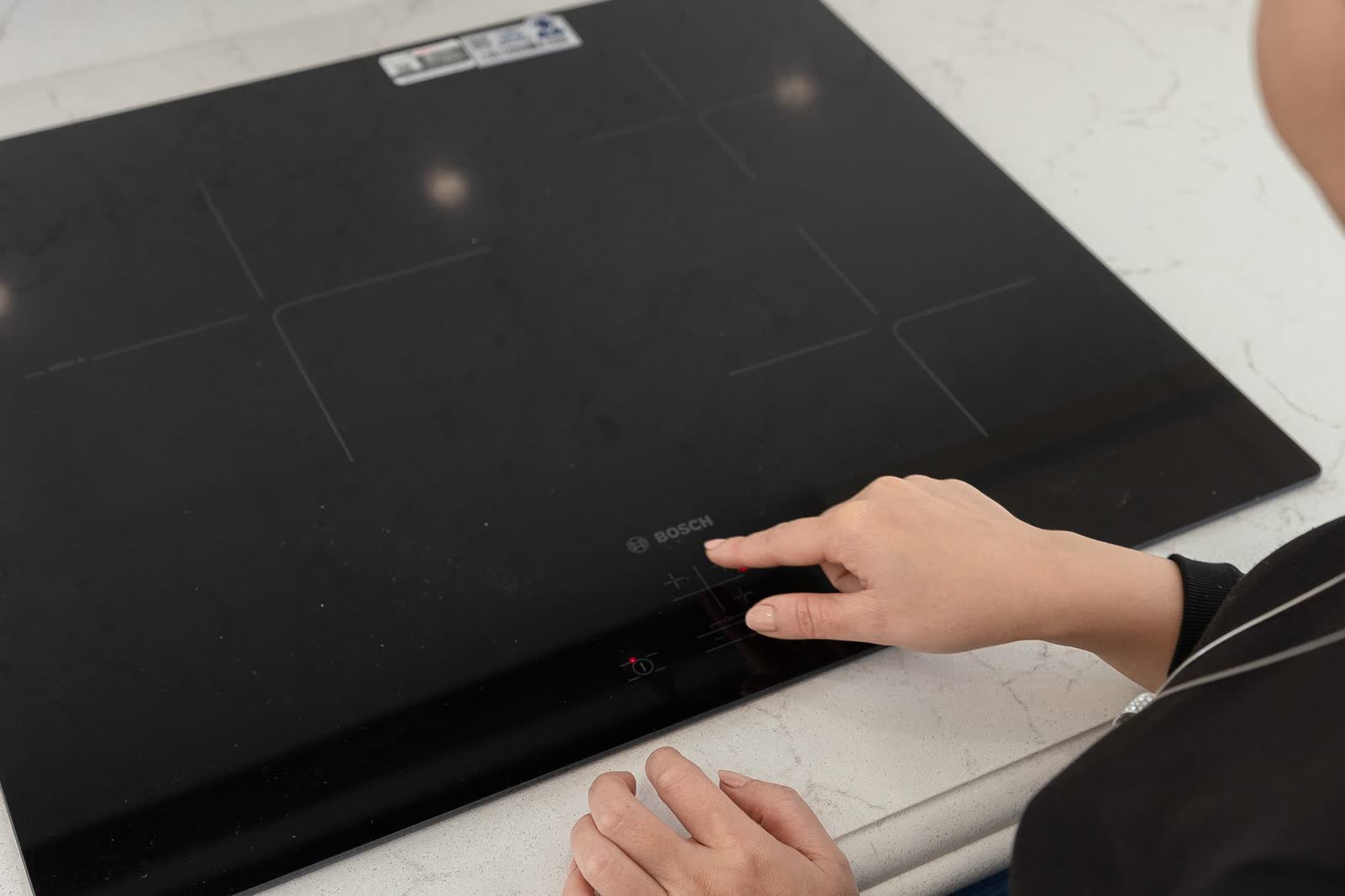 Hand pressing the touch controls of a black induction cooktop