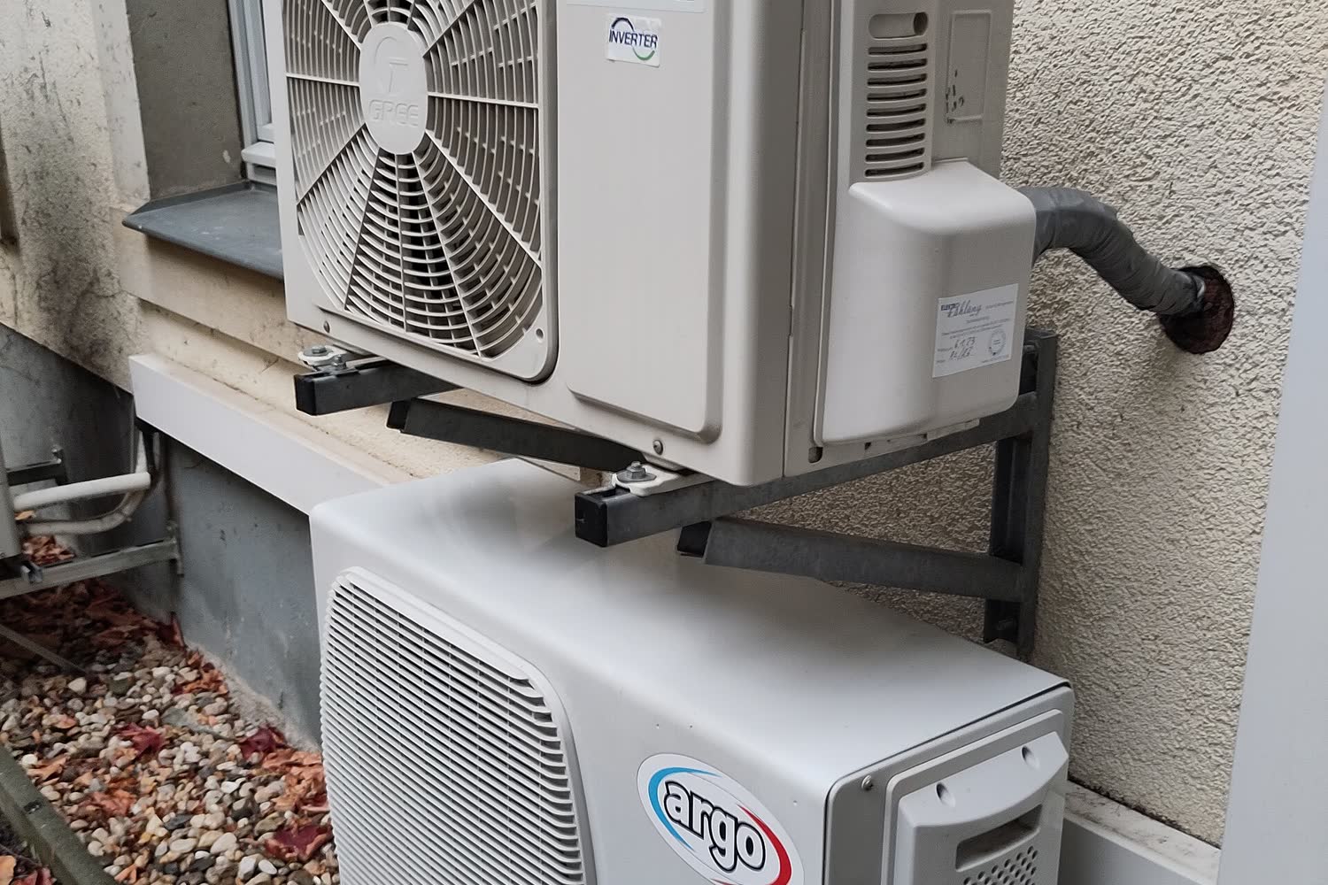 Two ductless mini-split outdoor units on a house wall, one on a steel wall bracket, with the insulated line set running into the wall