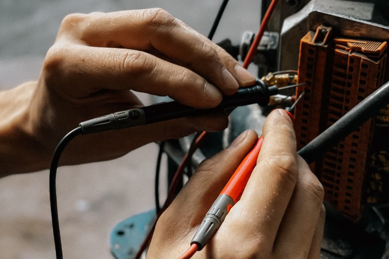 Hands holding multimeter probes on motor wiring terminals