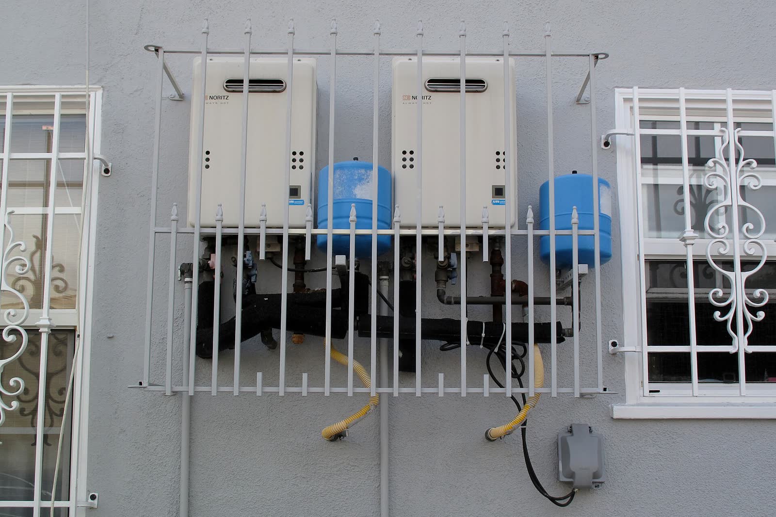 Two wall-mounted tankless water heaters with expansion tanks on an exterior wall
