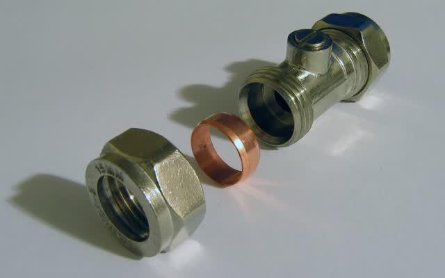 Compression fitting taken apart: nut, ferrule (olive) and valve body, the parts that seal a supply line without solder