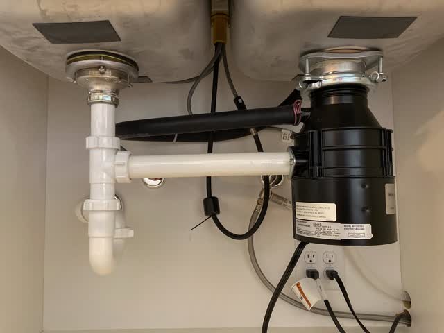 Garbage disposal mounted under a kitchen sink with its drain trap and plumbing
