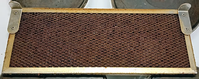 Aluminum mesh grease filter from an under-cabinet range hood, clogged brown with years of grease; a filter this loaded cuts airflow and is a fire risk