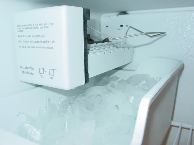 Refrigerator freezer ice maker module with the shut-off arm raised over the ice bin