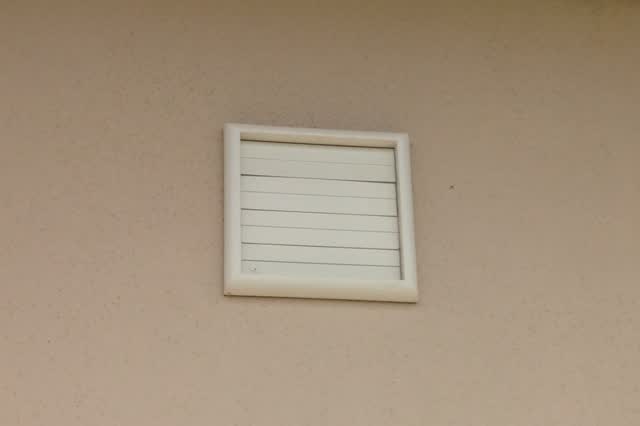 Louvered gravity-damper (shutter) vent cap on a wall at the end of a kitchen exhaust duct; the louvers should swing open freely when the fan runs