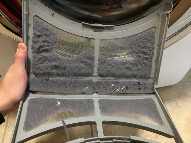 Fold-open dryer lint screen caked with lint on every panel, the kind of buildup that restricts airflow and slows drying