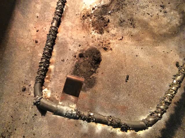 Failed oven bake element on the oven floor: the sheath burned through and blistered where it shorted, with scorch marks on the enamel around it