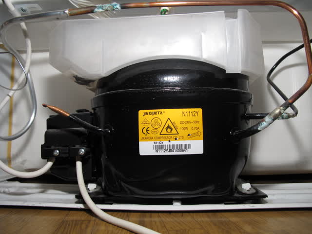 Small refrigerator compressor with the start relay and overload housing plugged onto its side terminals, power cord entering the relay cover