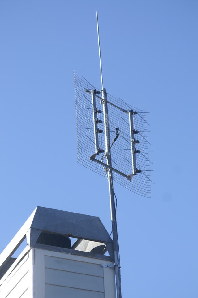 Outdoor UHF TV antenna (bowtie array with a mesh reflector) on a mast strapped to the chimney of a house