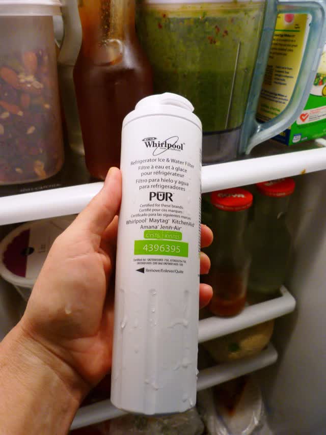 Replacement refrigerator water filter cartridge held up inside a fridge