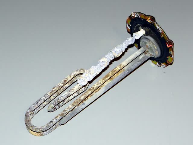 Electric water heater element pulled from a tank, crusted with mineral scale, next to a magnesium anode eaten down to its core wire (flange-mount style used on small tanks)