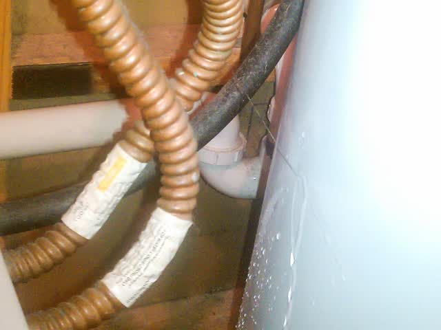 Water beading and running down the side of a water heater tank below corrugated copper flex connectors, the kind of wet spot to trace back to its source before condemning the tank